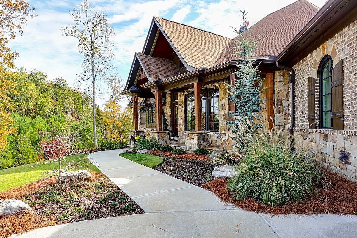 House plan exterior featuring stone and brick facade, prominent gables, and timber porch supports.
