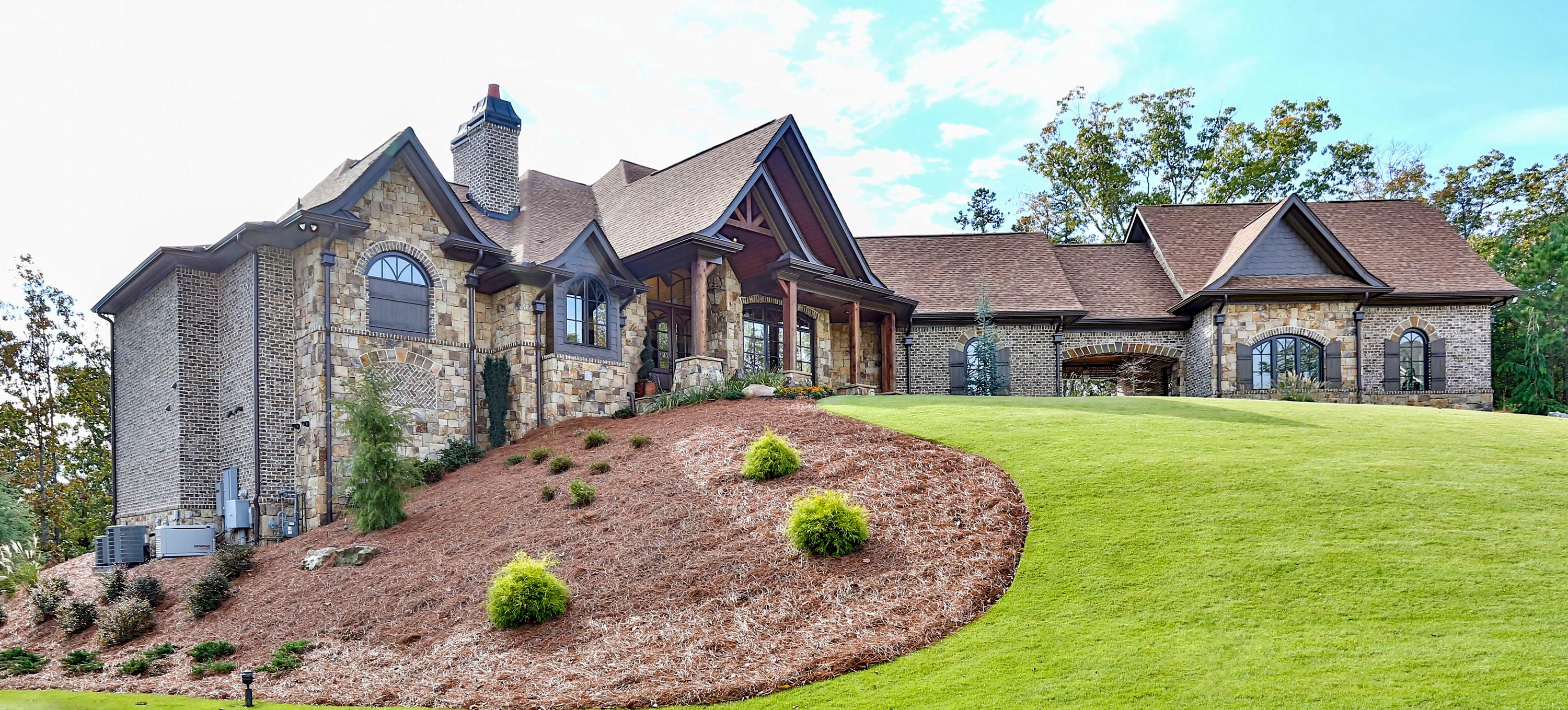 House plan exterior with stone and brick facade, prominent gables, arched windows, and a covered entry porch.