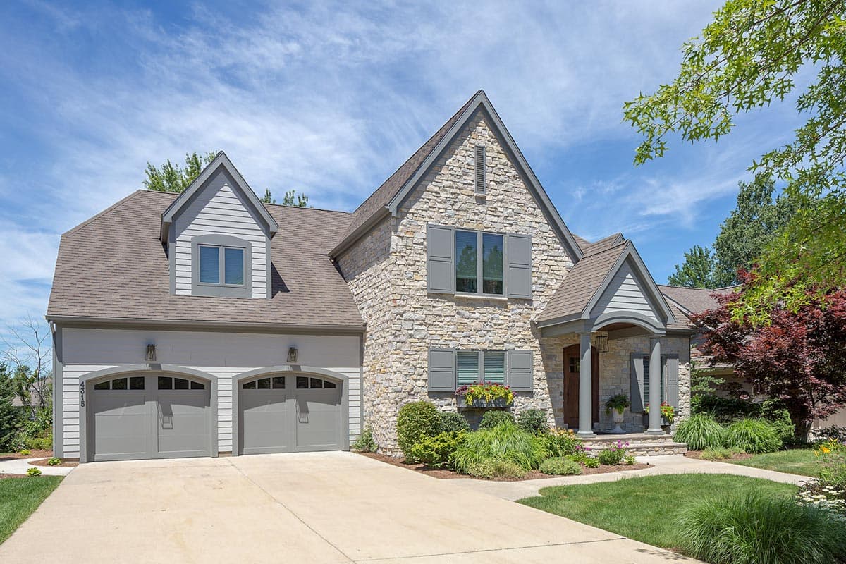 House plan exterior: Two-story stone and siding home with a covered entry porch, dormers, and a three-car garage.