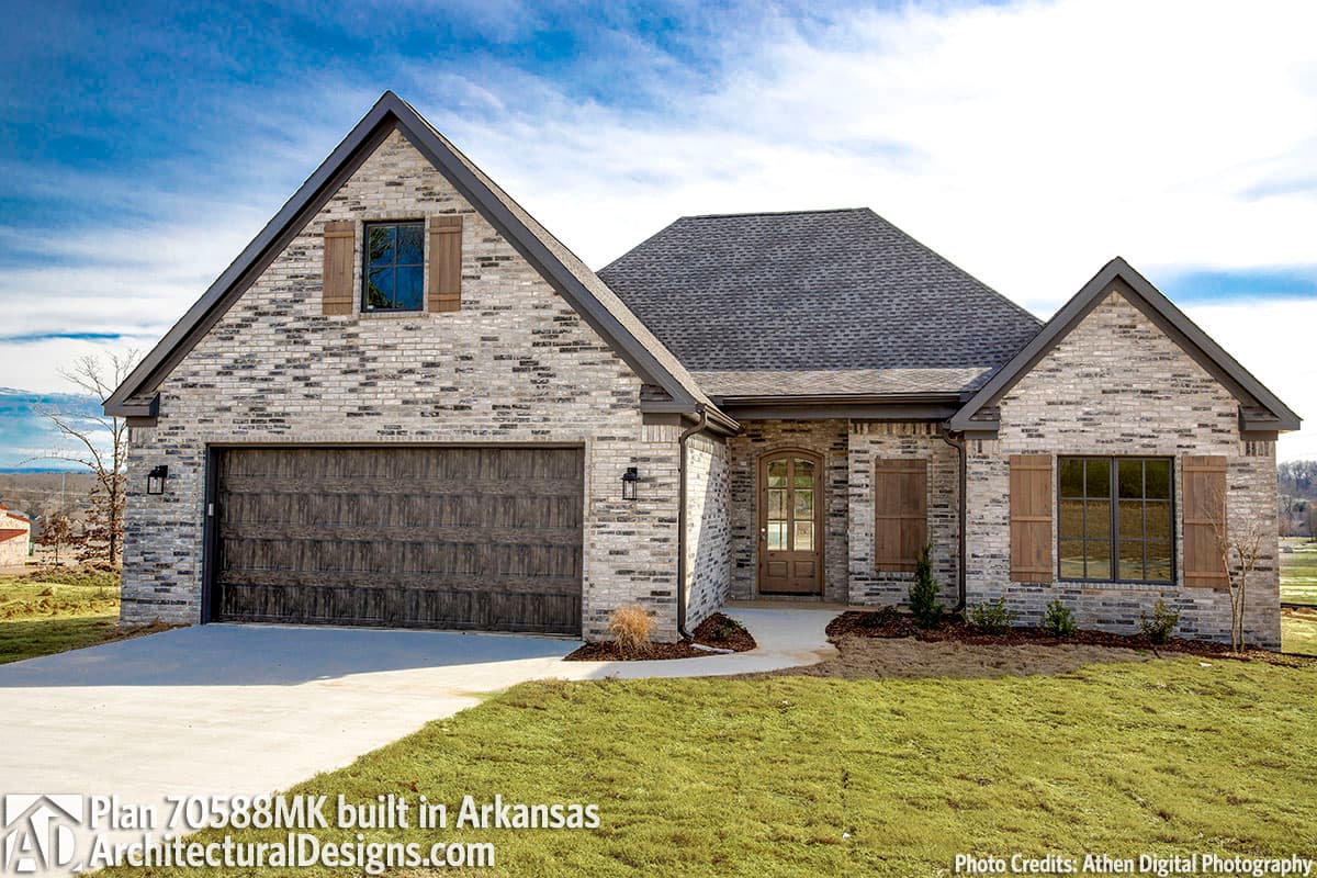 House plan exterior: One-story home with brick facade, gable rooflines, wood garage door, and arched entry.