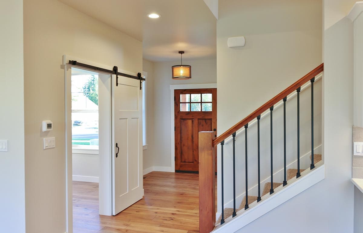 Interior view of home entryway with a wooden front door, sliding barn door, and staircase with wood railing and black spindles.