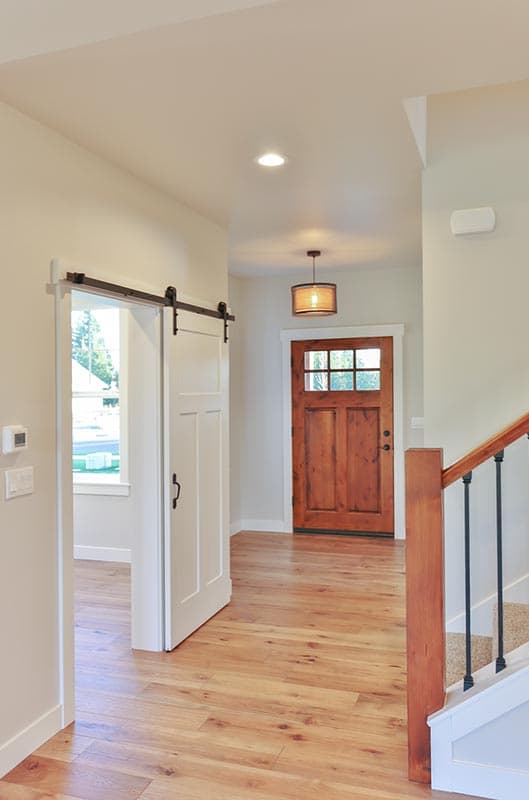 Interior view of a house entryway with a wooden front door, a sliding barn door, and a staircase.