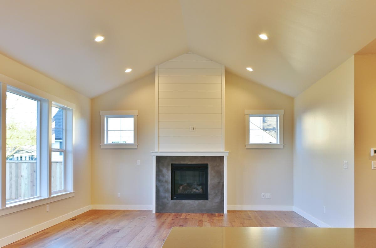 Interior view of a great room with vaulted ceiling, fireplace with shiplap surround, and large windows.
