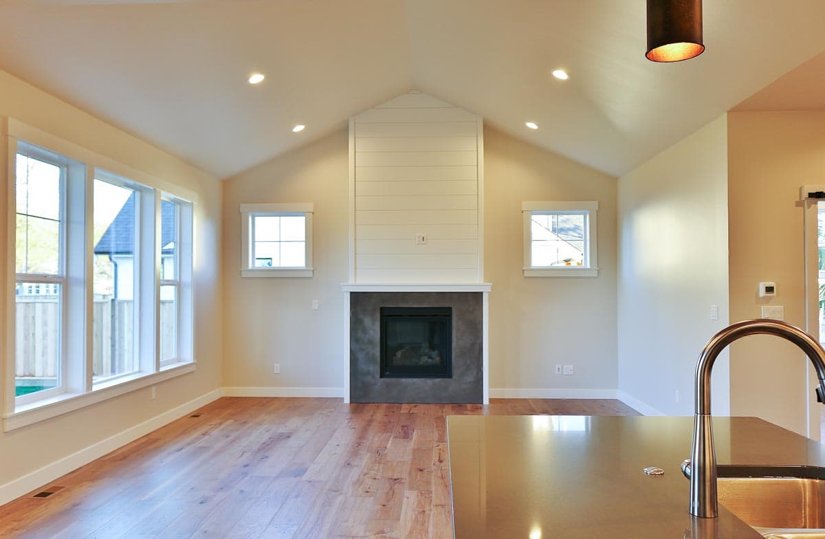 Living room interior with vaulted ceiling, fireplace, shiplap accent, and large windows.