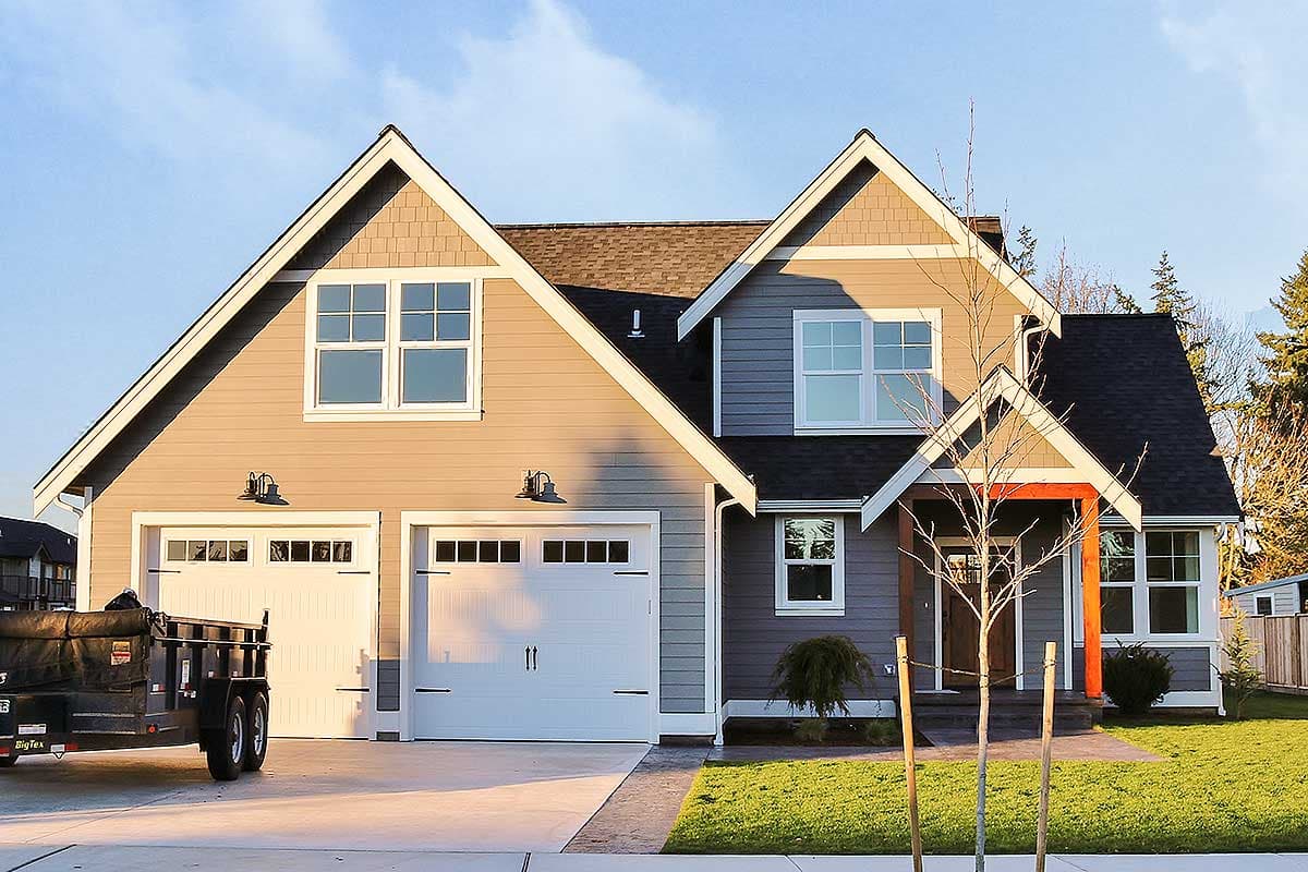 House plan exterior: Two-story dwelling with a two-car garage, prominent gables, shingle siding accents, and a covered entrance with wood beams.
