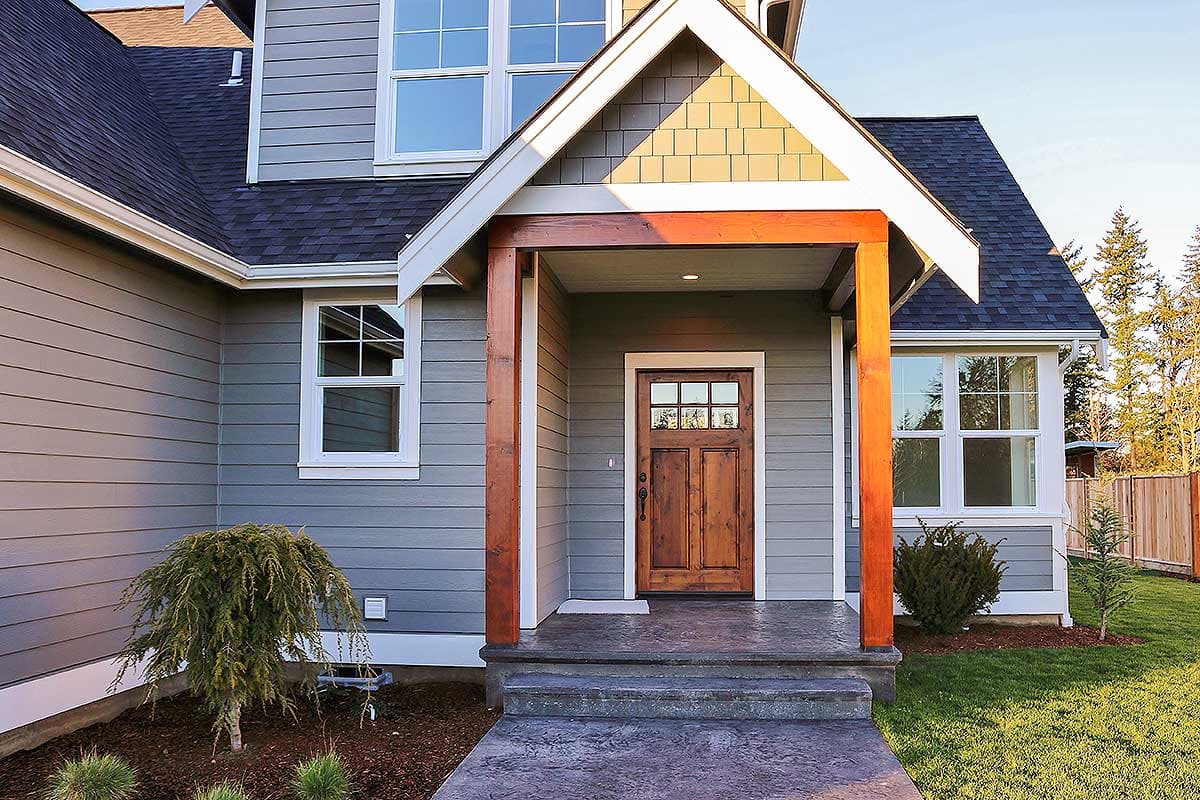 House plan exterior: Two-story home with covered entryway, wooden front door with glass panes, and horizontal siding.