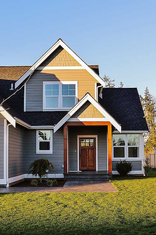 House plan exterior: Two-story home with prominent gabled dormer, covered entryway with wood posts, and multi-pane entry door.