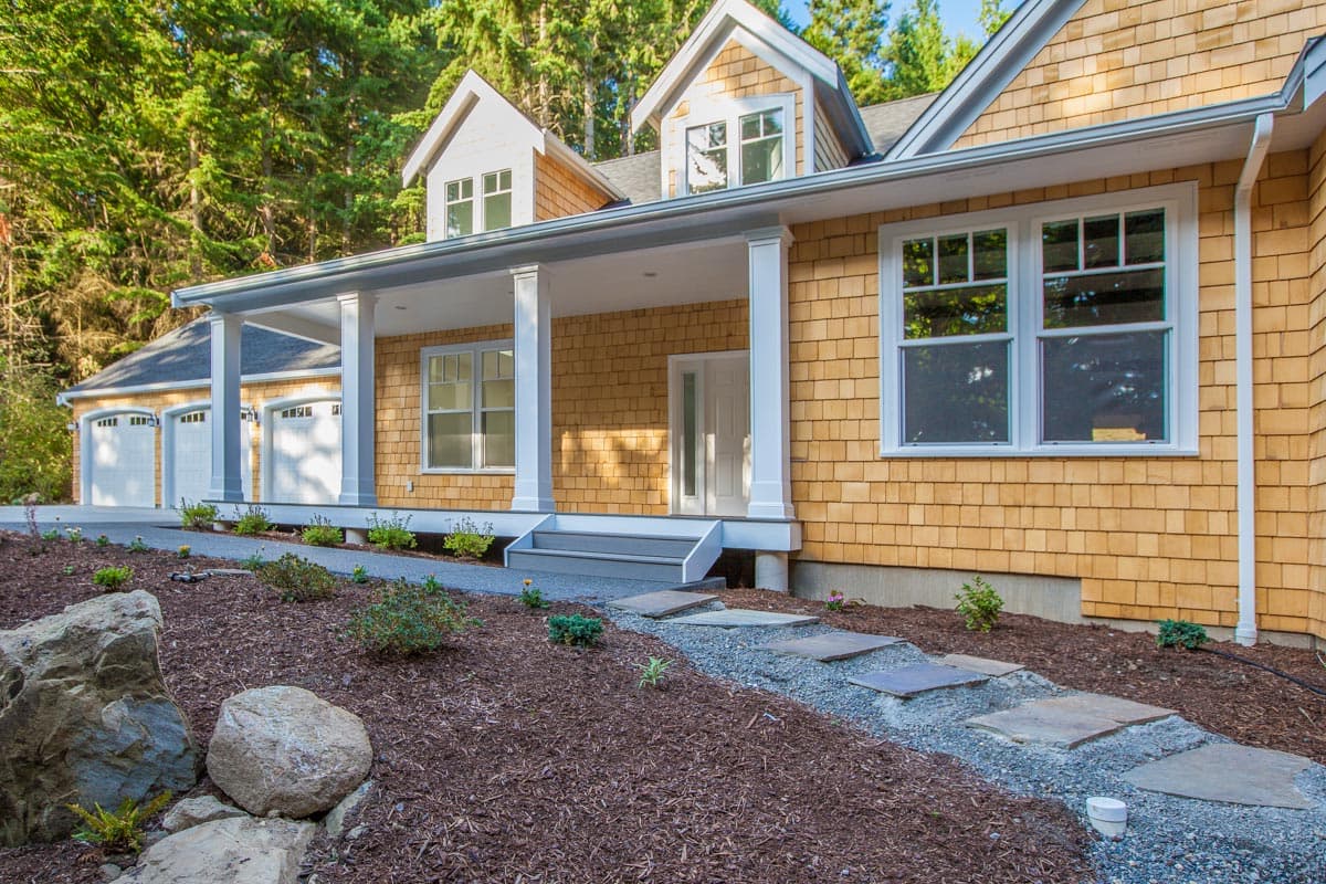 House plan exterior with cedar shingles, covered porch, dormers, and three-car garage.