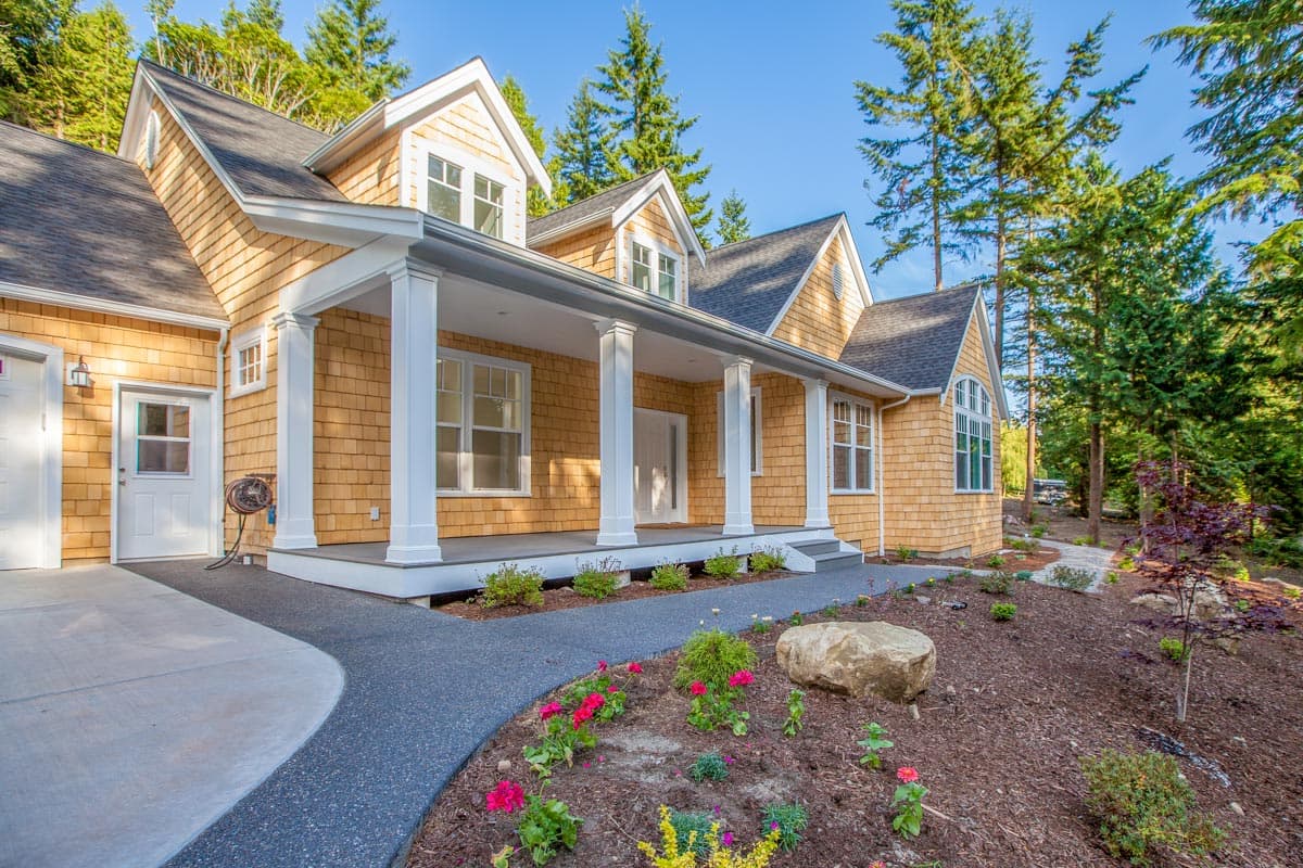 House plan exterior. Two-story with cedar shake siding. Features include a covered porch with columns, gabled dormers, and a prominent roofline.