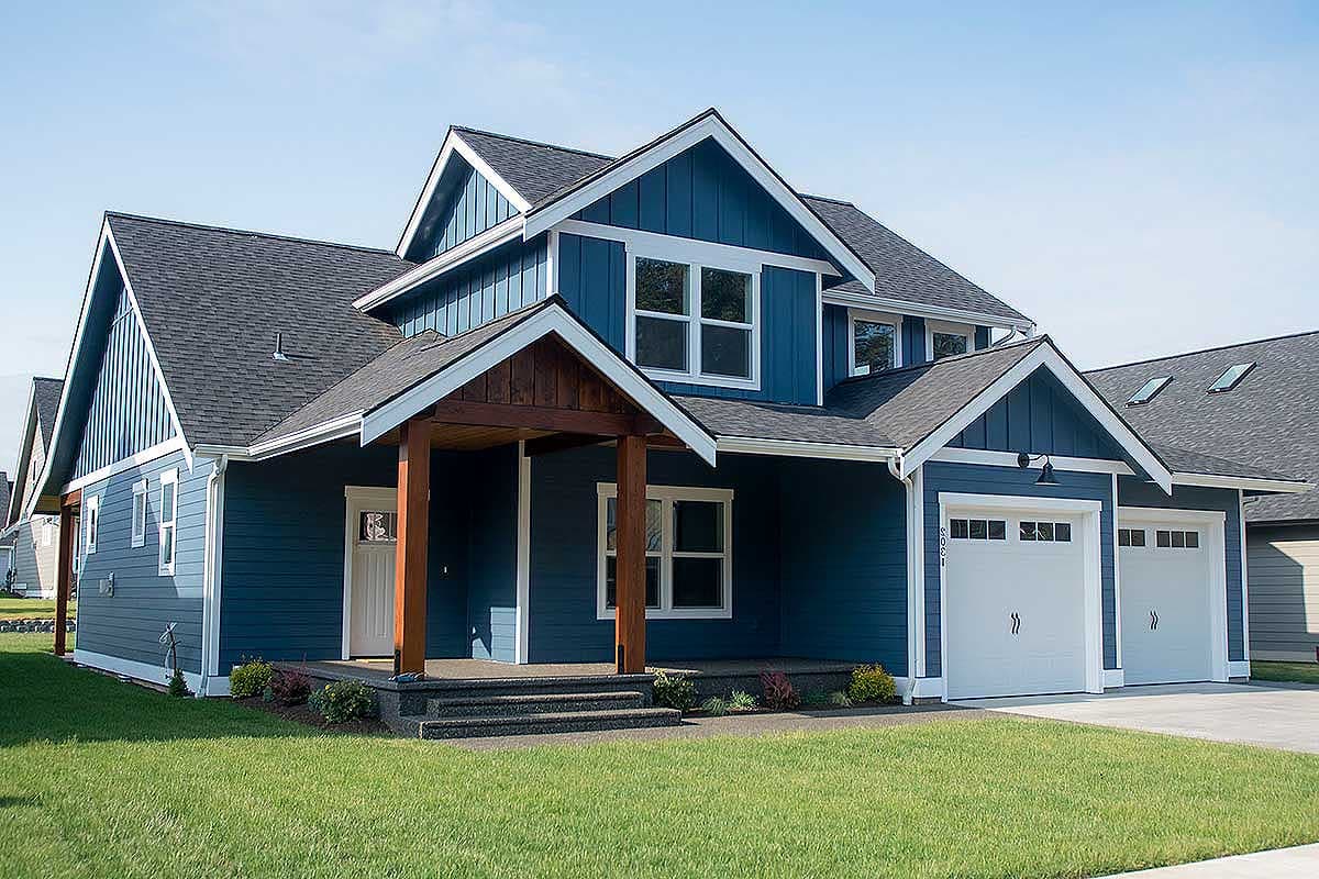 House plan exterior. Two-story home with a gabled roof, covered entry porch, and two-car garage. Vertical siding on the facade.