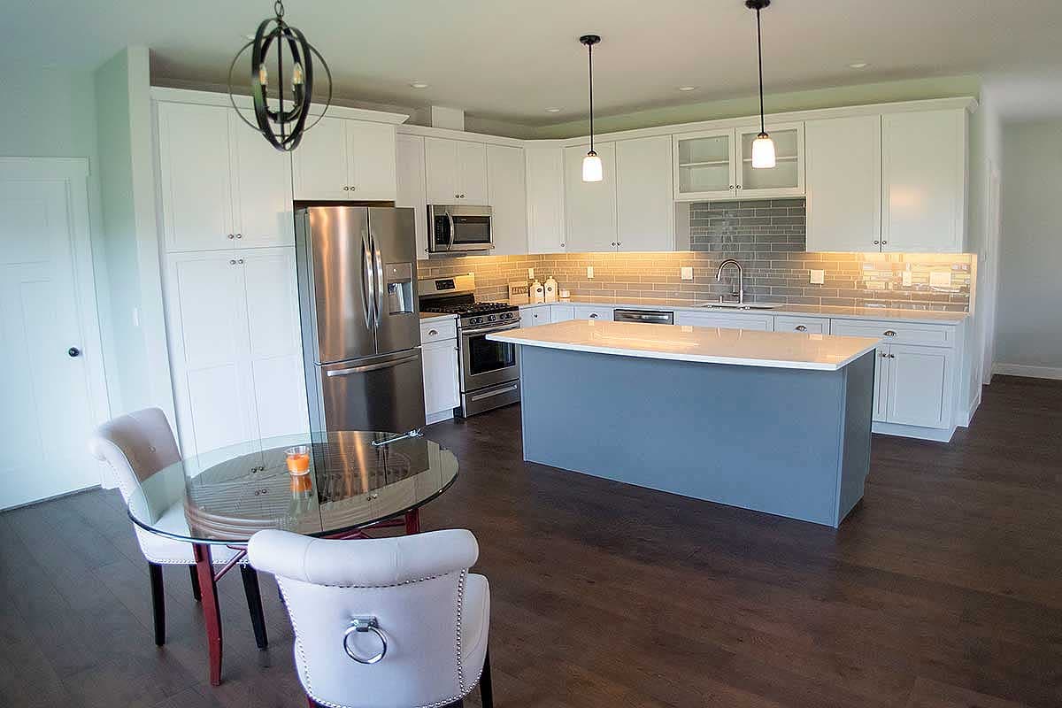Kitchen with white cabinetry, stainless steel appliances, gray subway tile backsplash, and a blue island.