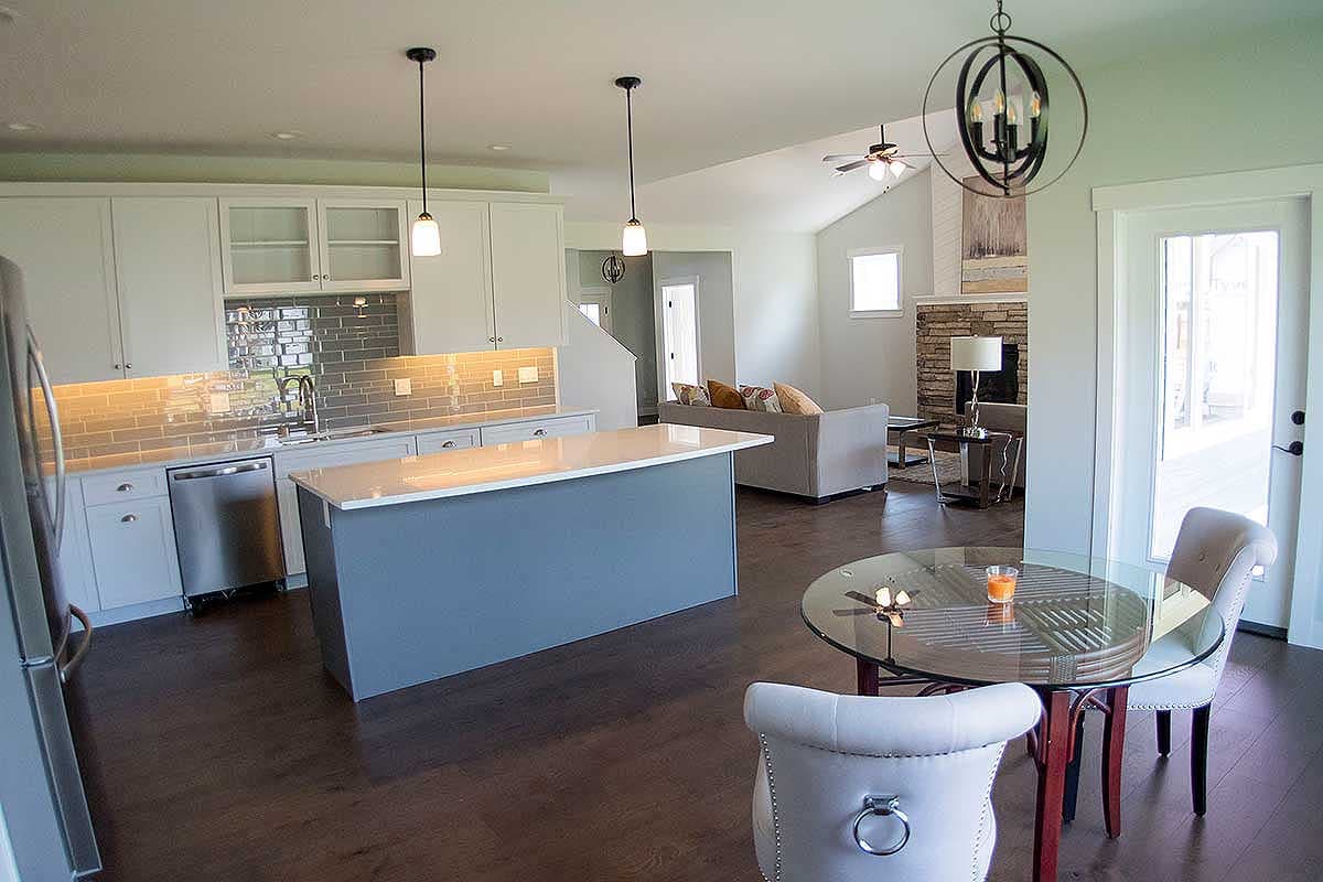 Interior view of an open-concept kitchen and living area with a central island, stone fireplace, and vaulted ceiling.