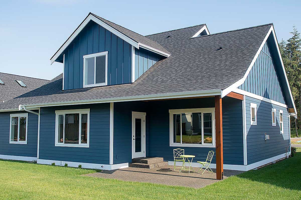 House plan exterior with blue vertical siding, dark asphalt roof, covered patio with two windows, and gabled dormers.