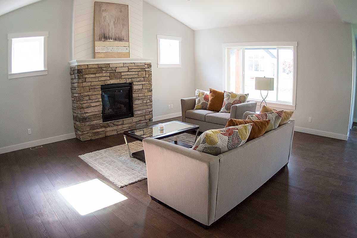Living room with vaulted ceiling, stone fireplace, and two sofas. Wide window provides natural light.