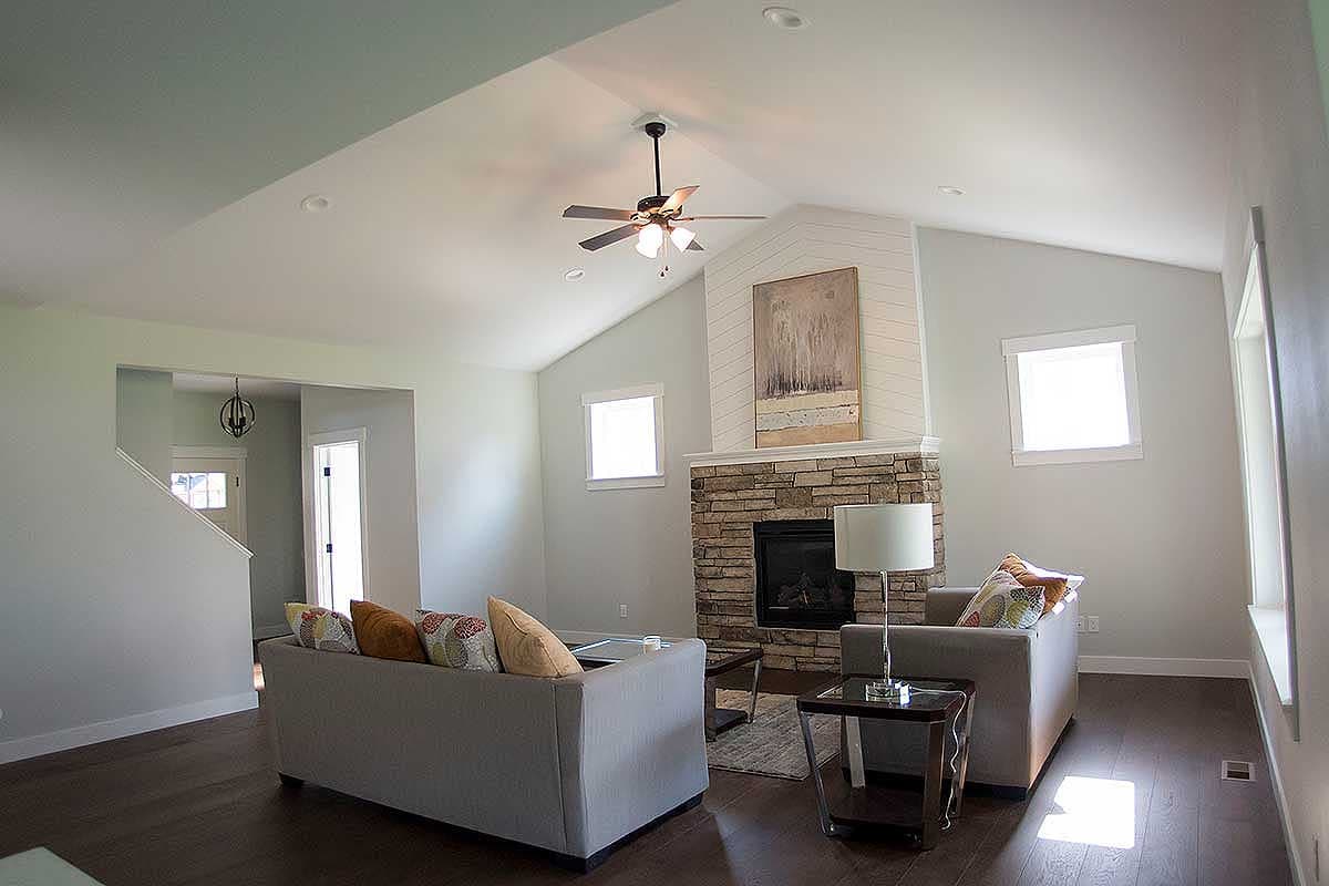 Living room with vaulted ceiling, stone fireplace, and open entrance to staircase and hallway.