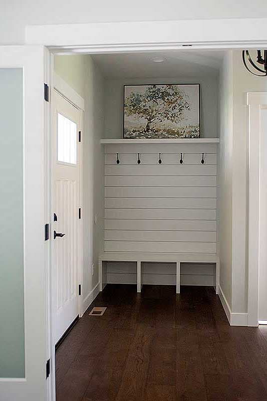 Mudroom interior with built-in bench, shiplap wall, coat hooks, and artwork above.