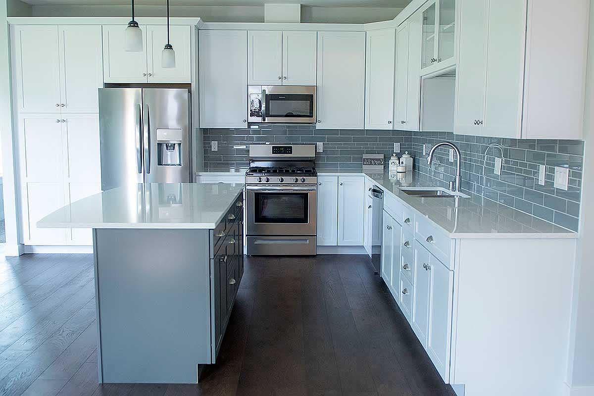 Modern kitchen with white shaker cabinets, stainless steel appliances, quartz countertops, and a gray island.