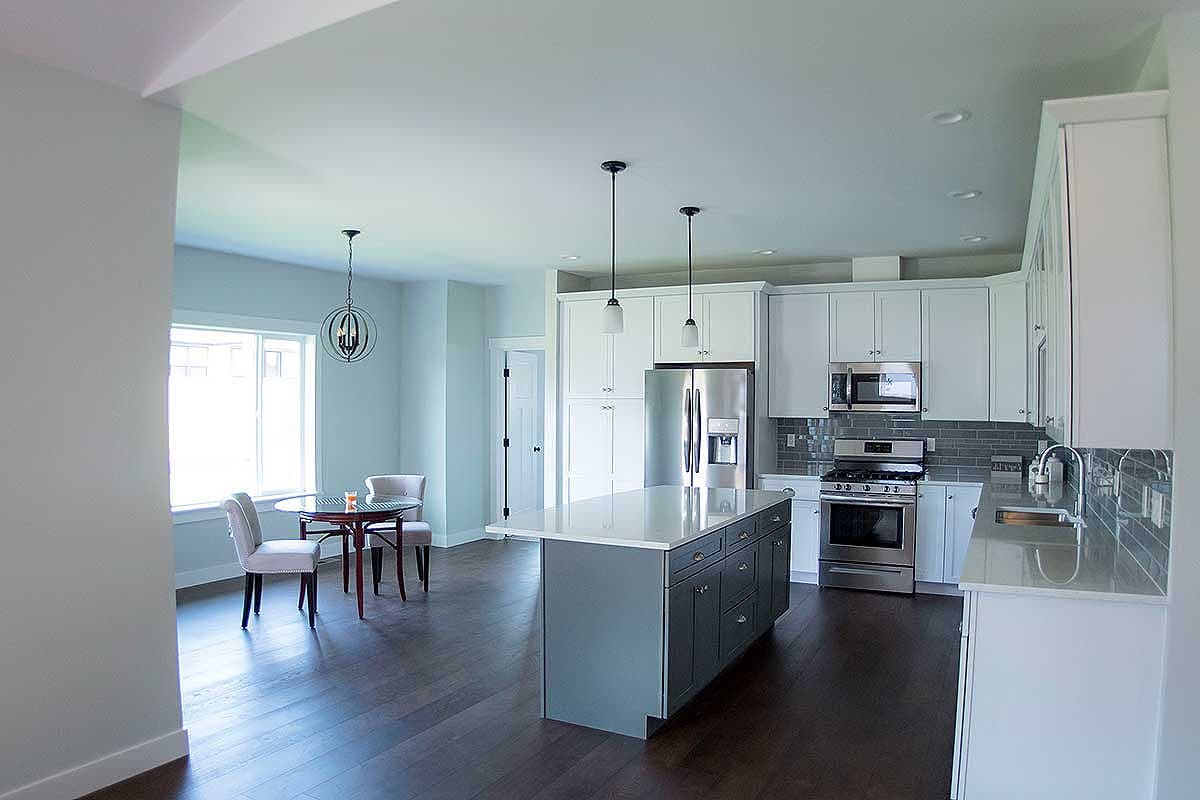 Open-concept kitchen with island, stainless steel appliances, gray tile backsplash, and adjacent dining area with table and chairs.