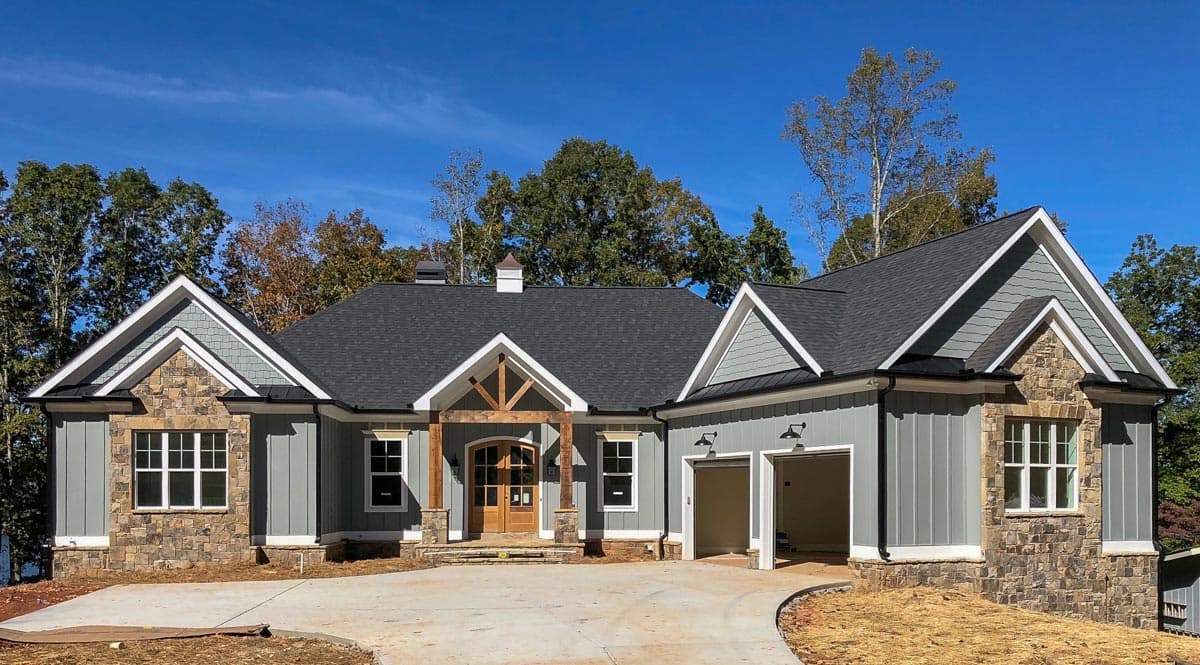 House plan exterior: One-story Modern Farmhouse with stone accents, gables, prominent timber-framed entry, and a side-facing two-car garage.