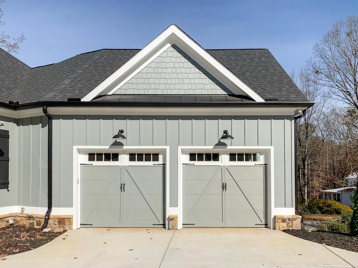 House plan exterior: Two-car garage with vertical siding, gable dormer, and decorative barn-style doors.