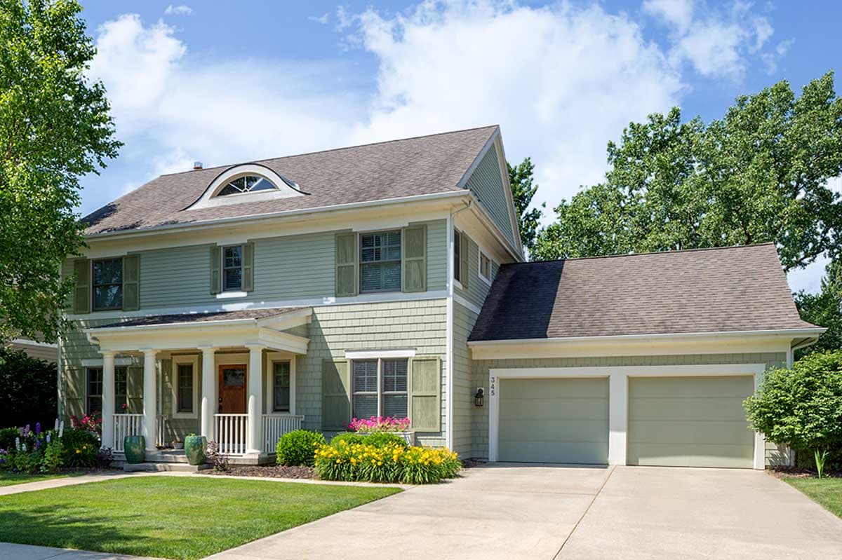 House plan exterior. Two-story home with Craftsman-style elements. Features a front porch with columns, a dormer, and an attached two-car garage.