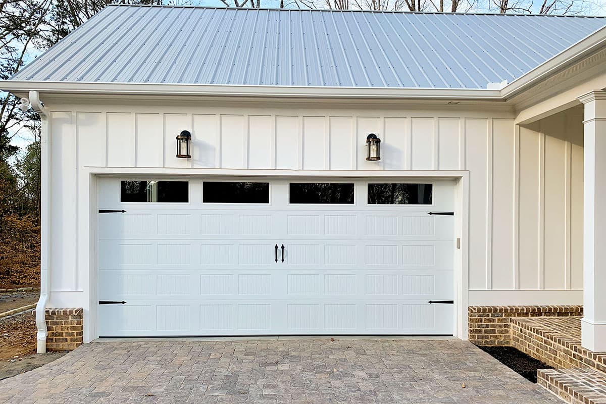 House plan exterior showing a white garage door with windows, board and batten siding, and a standing seam metal roof.