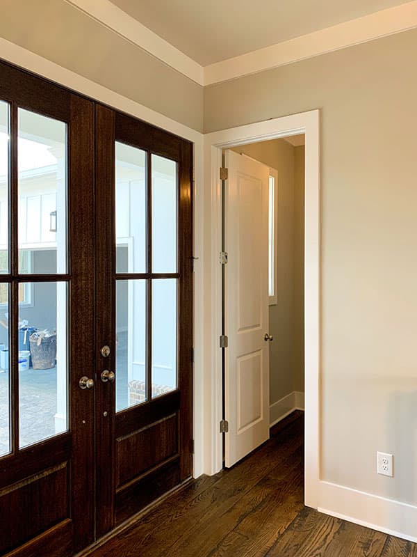 Interior view of double dark wood doors with glass panes and a white interior door ajar.