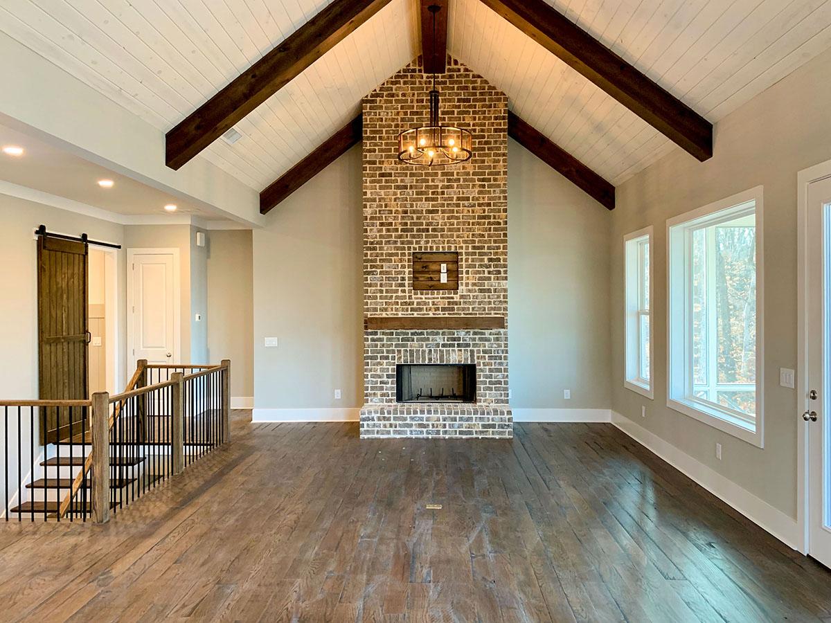Great room interior with vaulted ceiling, exposed beams, brick fireplace, and sliding barn door.