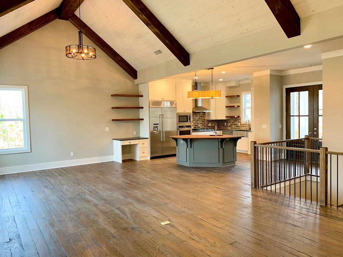 Vaulted living area with exposed beams opens to a kitchen with island, stainless steel appliances and brick backsplash.