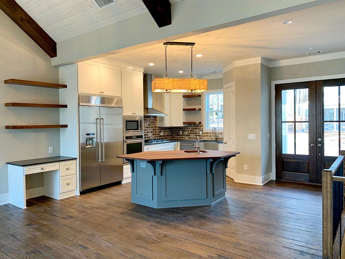 Open concept kitchen with vaulted beamed ceiling, island, stainless steel appliances, and double entry doors.