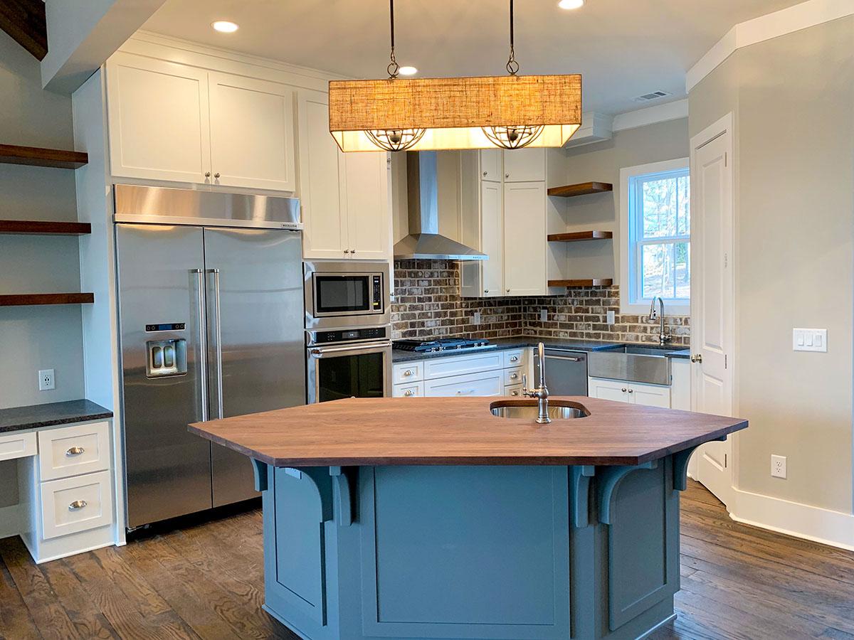 Kitchen featuring stainless steel appliances, white cabinets, subway tile backsplash, and a hexagonal island with a sink.