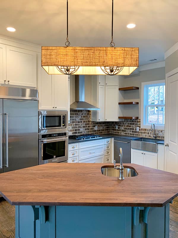 Kitchen with wood island, stainless steel appliances, brick backsplash, farmhouse sink, and pendant lighting.