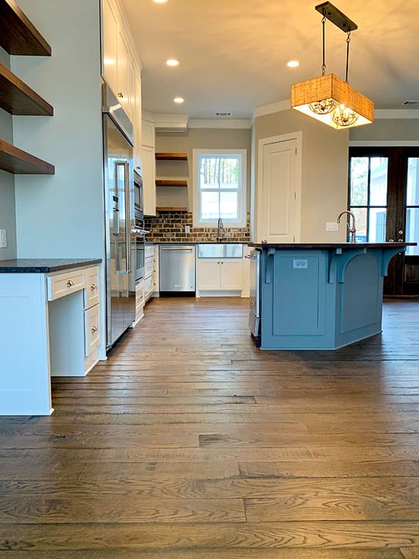 Kitchen with blue island, white cabinets, stainless steel appliances, farmhouse sink, brick backsplash, and wood floors.