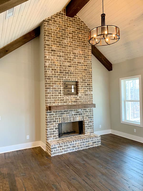 Great room interior with vaulted ceiling, exposed beams, and a floor-to-ceiling brick fireplace with wood mantel.