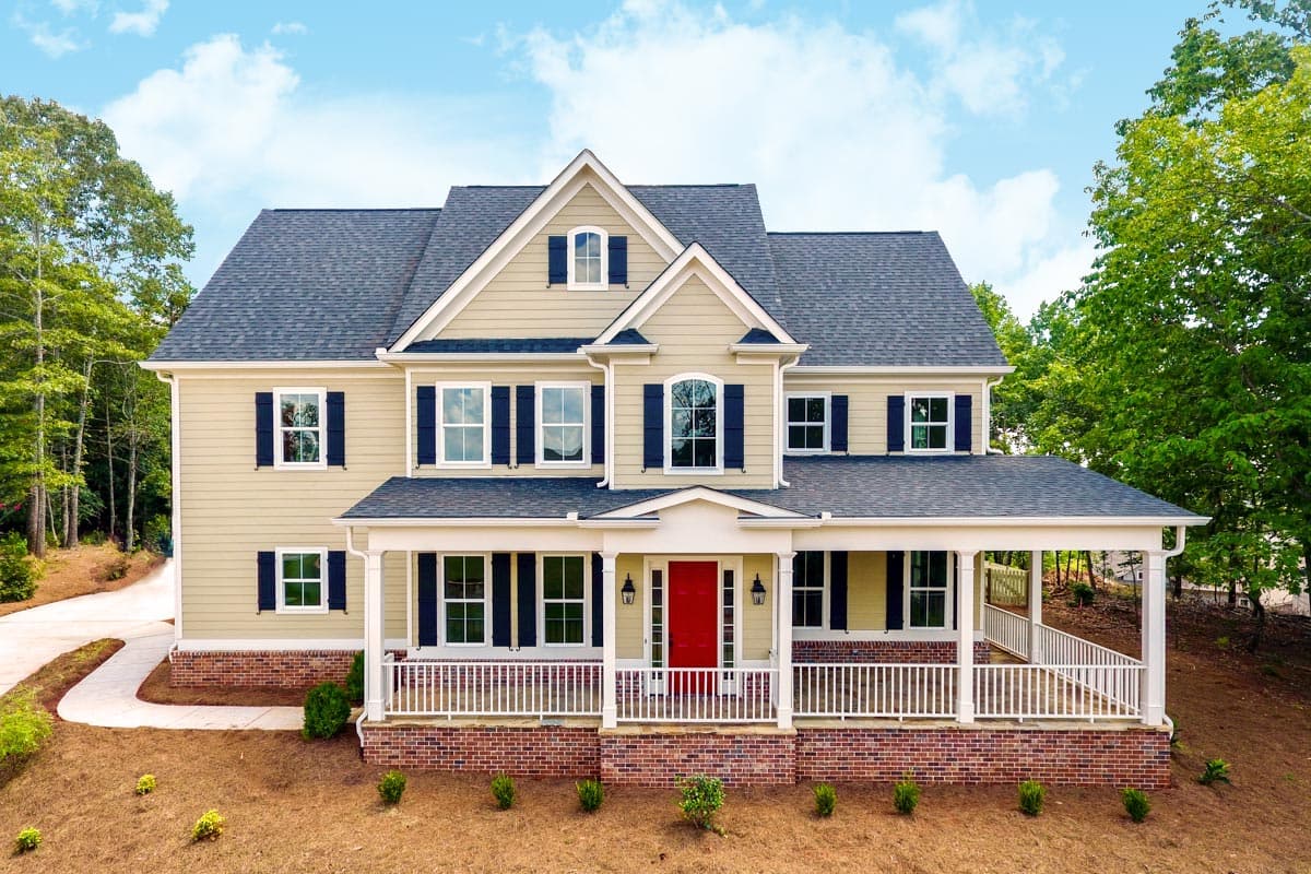 House plan exterior with two stories and a large front porch. Features include gables, dormers, and a brick foundation.