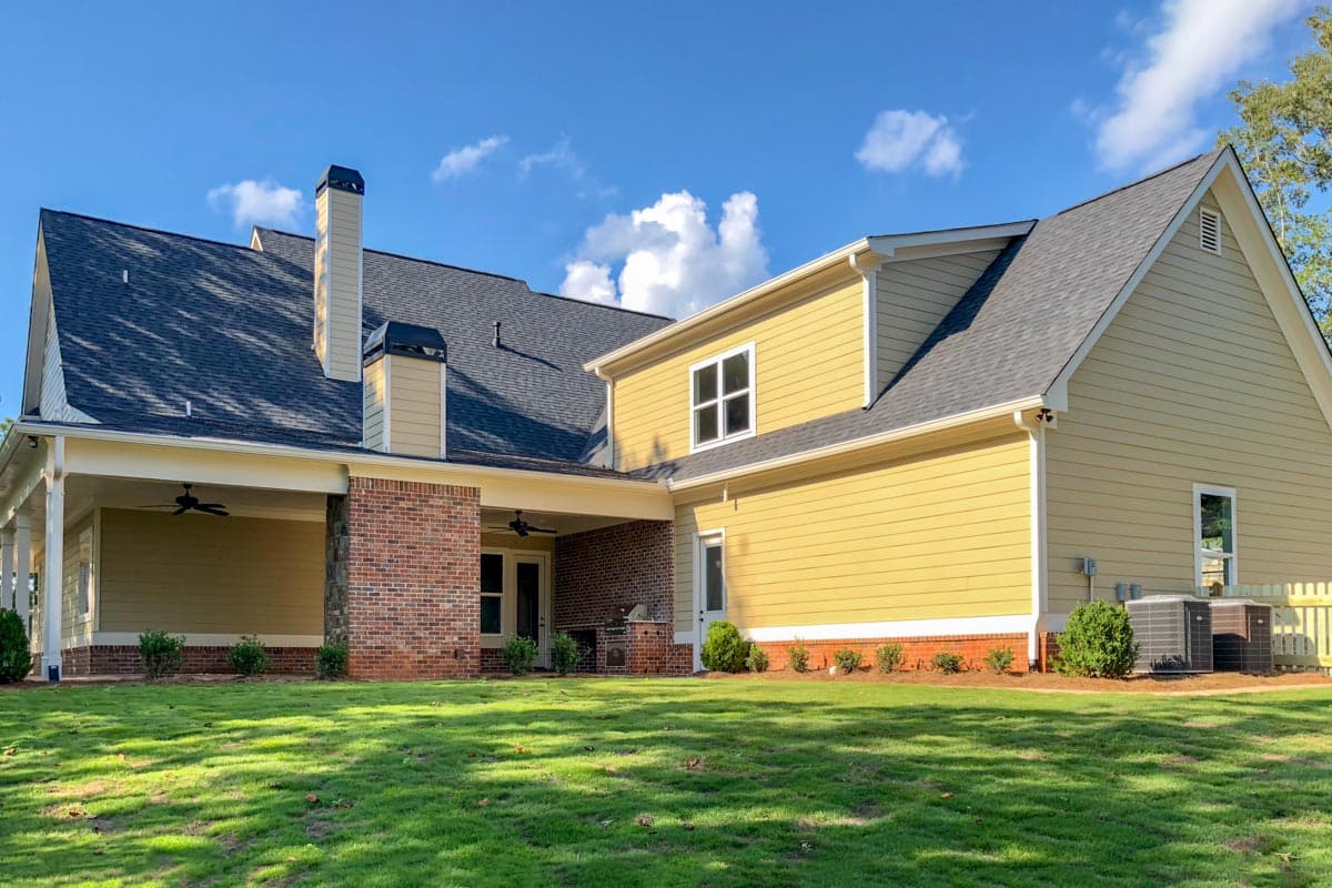 House plan exterior: Two-story home with a covered porch, brick accents, multiple gables, and a large chimney.
