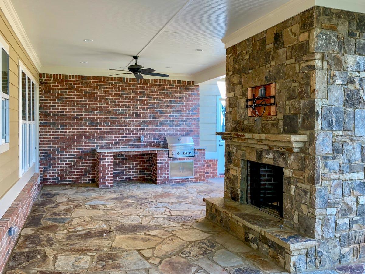 Covered patio with stone fireplace, built-in grill counter, brick wall, and ceiling fan.