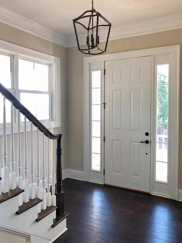 Interior view of house entrance showing white paneled door with sidelights, a staircase with white balusters, and a decorative lantern.