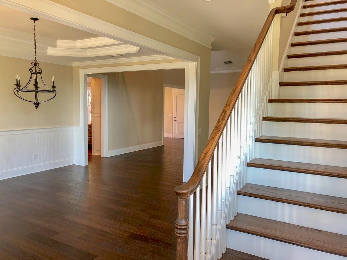 Interior view of a house entry with wood floors, a staircase with white balusters, and a tray ceiling with a chandelier.