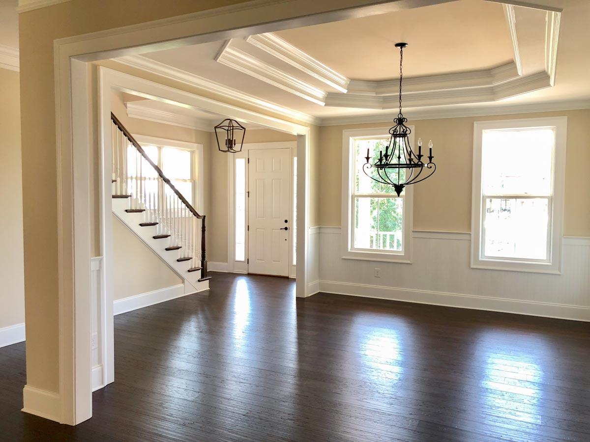 Interior view of a foyer with a staircase, wainscoting, a tray ceiling, and two chandeliers.