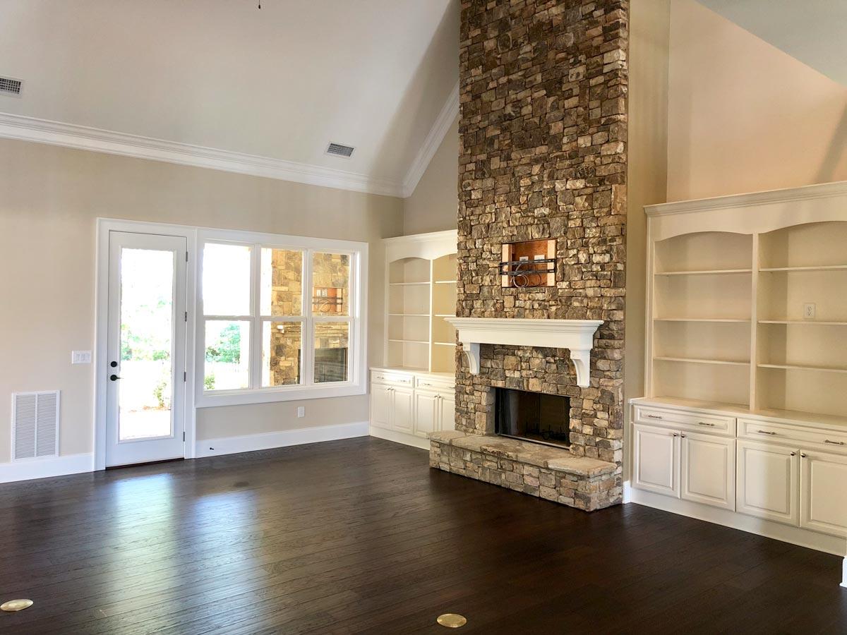 Interior view of a great room featuring a floor-to-ceiling stone fireplace, built-in bookshelves, and vaulted ceiling.