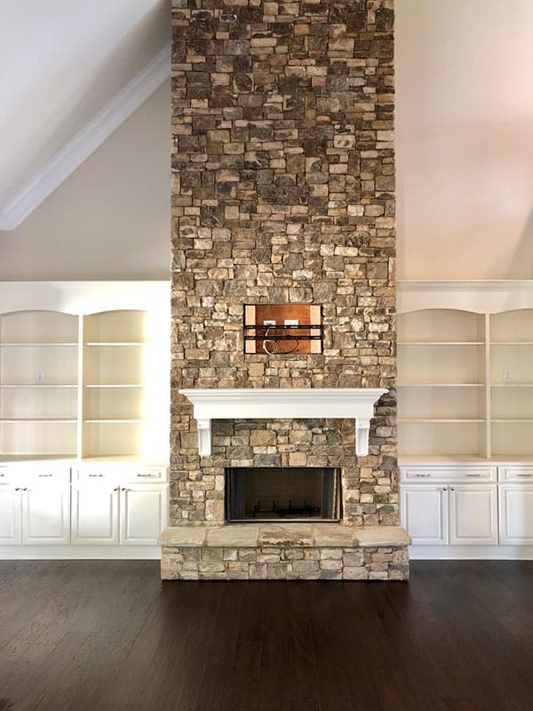 Interior view of a living room with a floor-to-ceiling stacked stone fireplace, built-in white cabinetry, and vaulted ceiling.