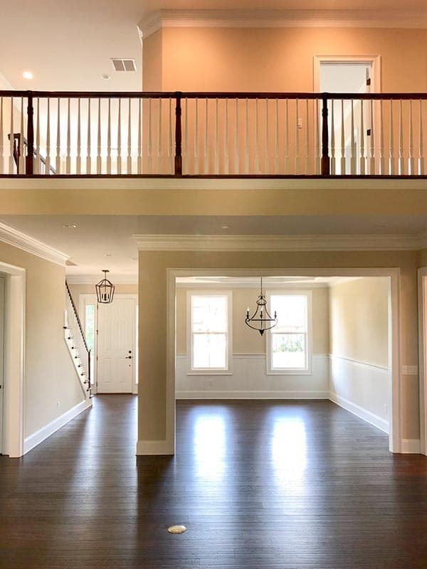 Interior view showing an open floor plan with a second-story railing, staircase, and formal dining area with windows.