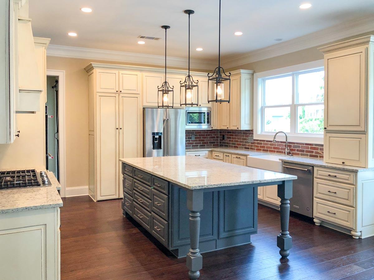 Kitchen with a large central island, white cabinetry, brick backsplash, stainless steel appliances, and pendant lighting.