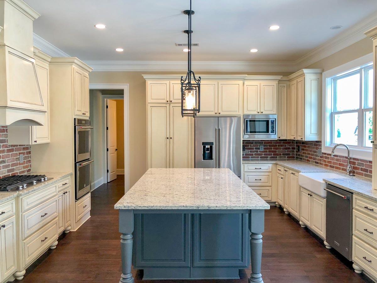 Kitchen interior with cream cabinetry, granite countertops, central island, double ovens, stainless steel appliances, and brick backsplash.