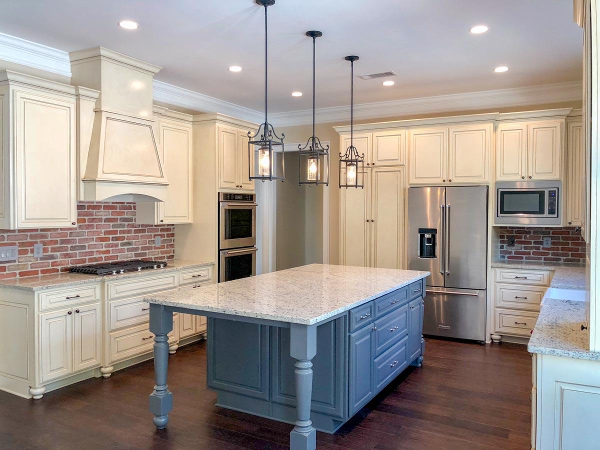 Kitchen featuring cream cabinetry, brick backsplash, stainless steel appliances, a large island with blue base cabinets, and pendant lighting.