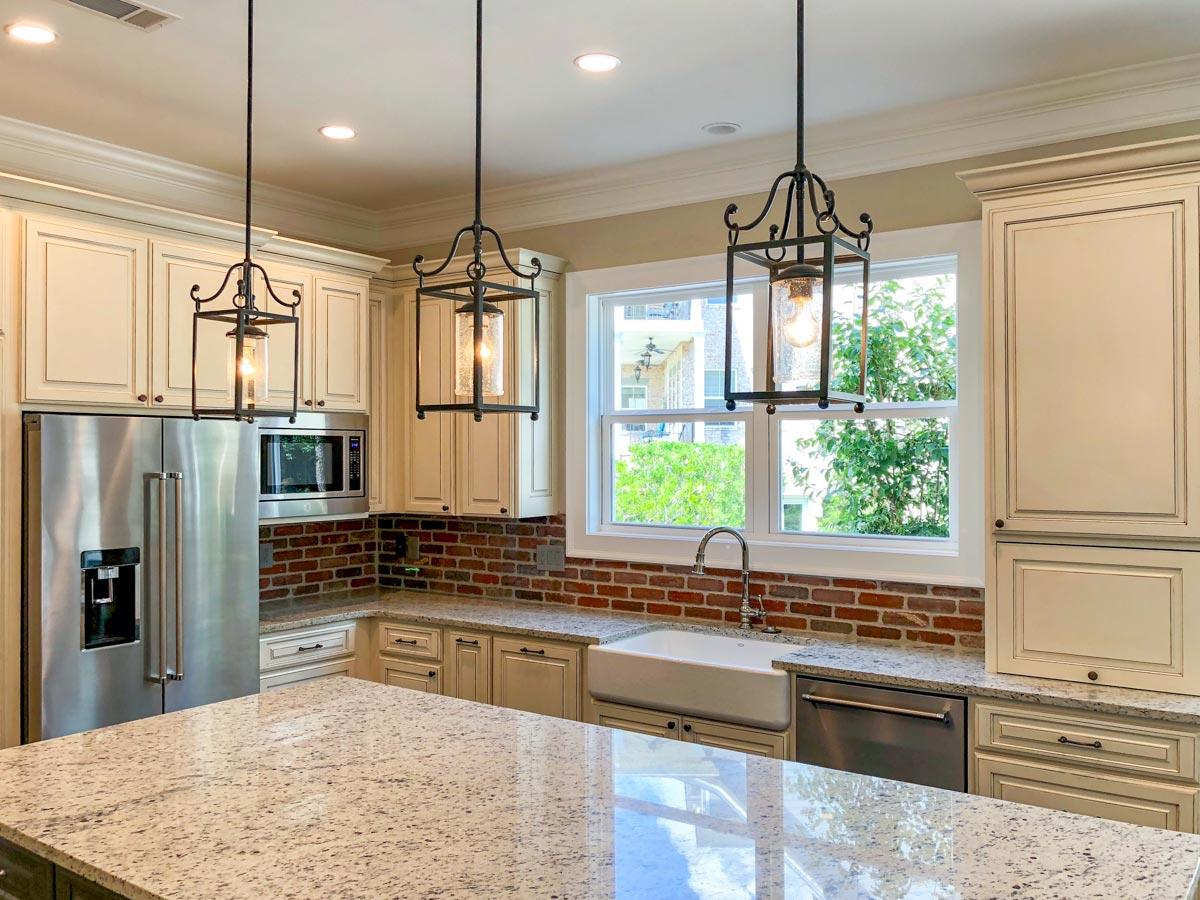 Kitchen with stainless steel refrigerator, inset cabinets, farmhouse sink, brick backsplash, and pendant lights.