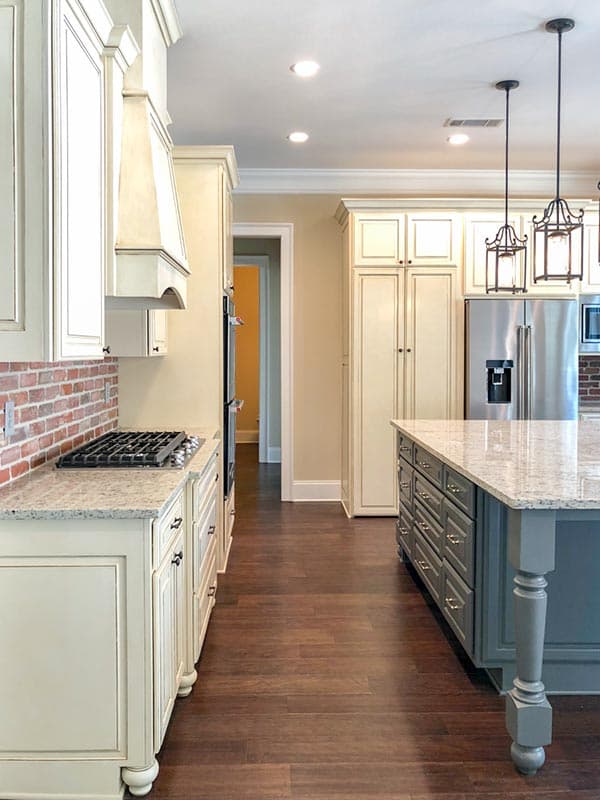 Kitchen with inset cabinetry, granite countertops, gas range, brick backsplash, and island with pendant lights.