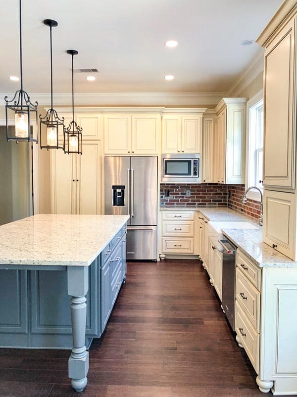 Kitchen featuring a large island with granite countertop, stainless steel appliances, white cabinetry, and brick backsplash.