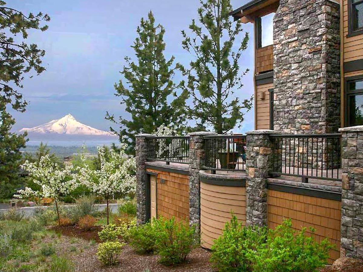 House plan exterior with stone chimney, wood siding, and covered balcony overlooking a snow-capped mountain.